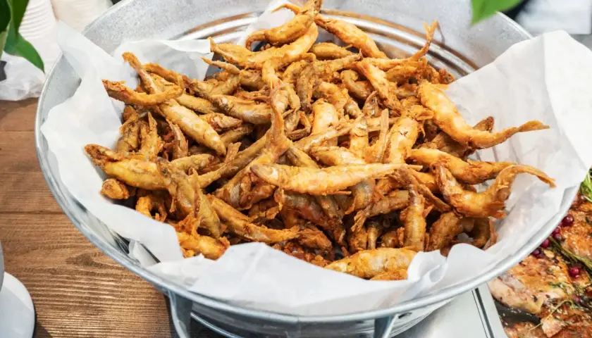 Un seau rempli d'éperlans frits dorés, prêts à être dégustés. Ces petits poissons croustillants sont un délice.