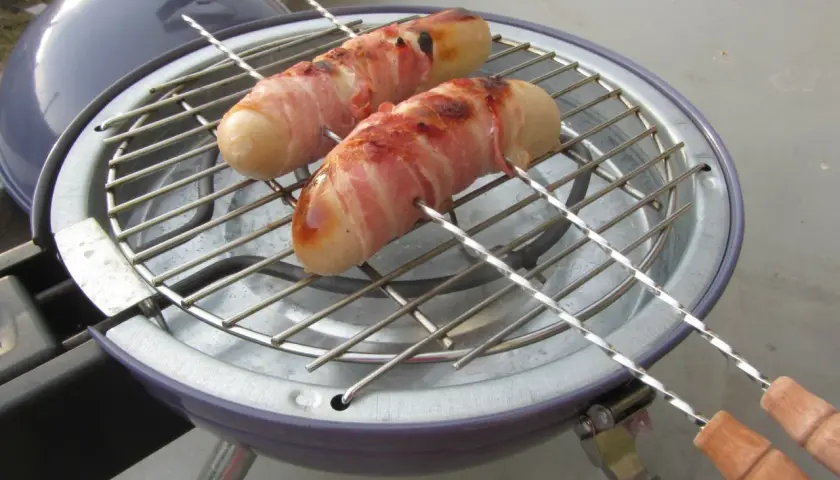 Deux boudins blancs enroulés de lard grillent sur un barbecue. Un délice pour un barbecue estival.