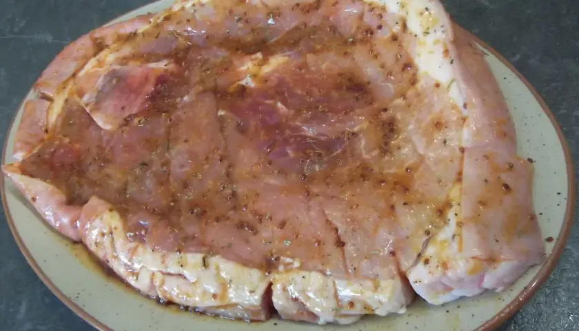 Rouelle de porc prête pour la plancha, généreusement recouverte d'une marinade savoureuse aux herbes et épices.