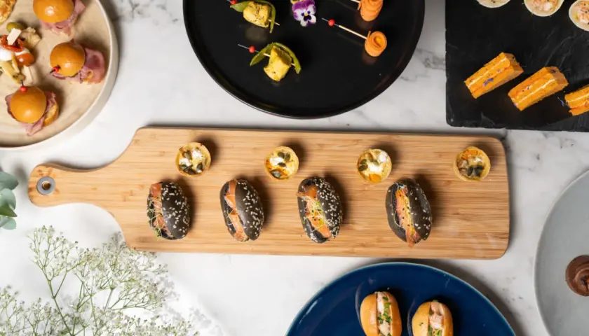 Assortiment de bouchées variées, parfaites pour un manger froid. Mini-burgers, tartes salées et sandwichs au saumon sur planche en bois.