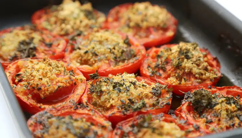 Tomates au barbecue, coupées en deux et garnies d'une chapelure dorée et d'herbes aromatiques, prêtes à être dégustées.