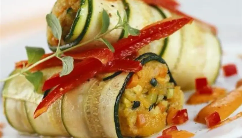 Rouleaux de courgette en lamelle garnis de légumes et de poivrons rouges, décorés d'herbes fraîches.