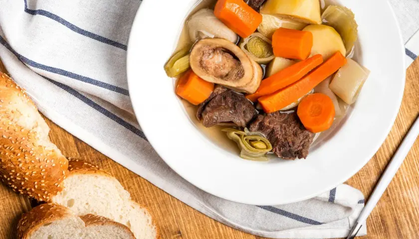 Un réconfortant pot-au-feu d'hiver avec du bœuf, des carottes, des poireaux et une os à moelle, servi avec du pain croustillant.