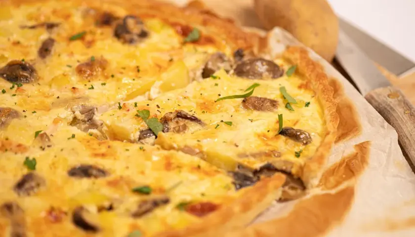 Une délicieuse quiche poulet pomme de terre, garnie de champignons et d'herbes fraîches, prête à être dégustée.