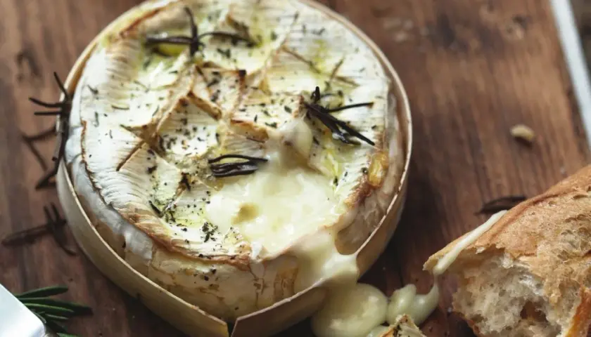 Un camembert au barbecue, fondant et parfumé au romarin, prêt à être dégusté avec une baguette croustillante.