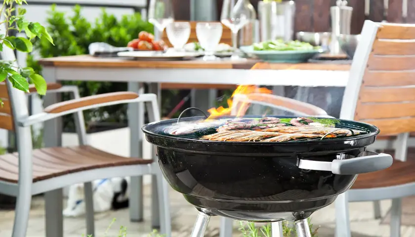 Un barbecue est allumé, des crevettes et du poisson grillent sur la grille. La table est dressée pour un repas en plein air.