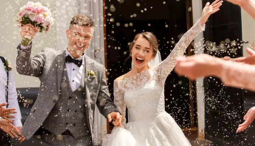 Jeune mariée et marié joyeux sortant de l'église sous une pluie de riz. Idées de mariage pour 20 personnes : une sortie mémorable !
