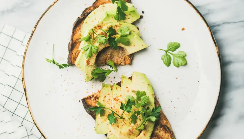 Deux toasts de pain grillé garnis de tranches d'avocat frais, parsemés d'épices et de persil. Une recette avocat simple et savoureuse.