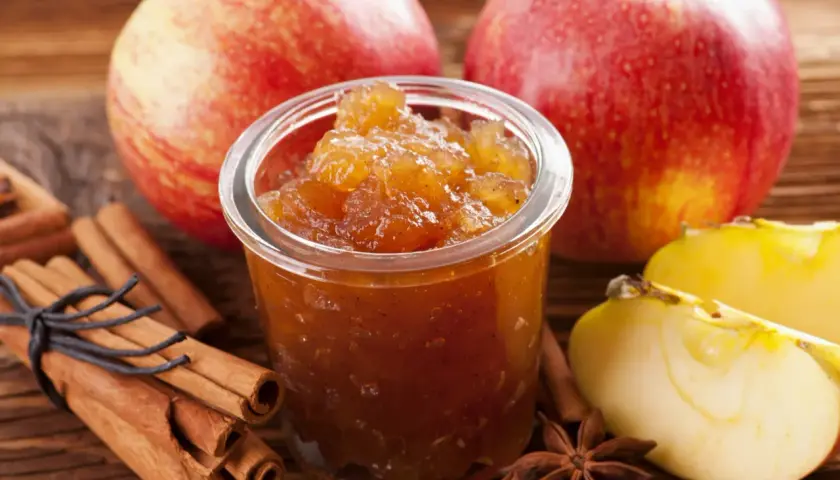 Un pot de confiture de pommes originales, avec des bâtons de cannelle, des étoiles de badiane et des pommes fraîches.