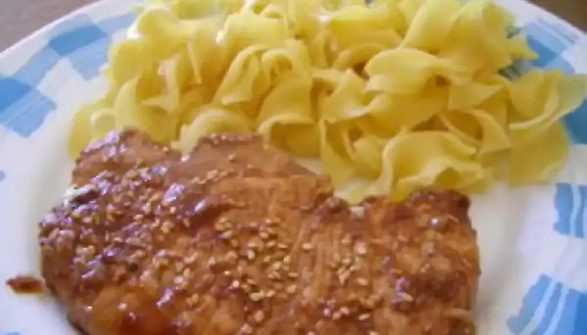 Une côte de porc savoureuse, nappée d'une sauce soja brillante et parsemée de graines de sésame, accompagnée de pâtes fraîches.