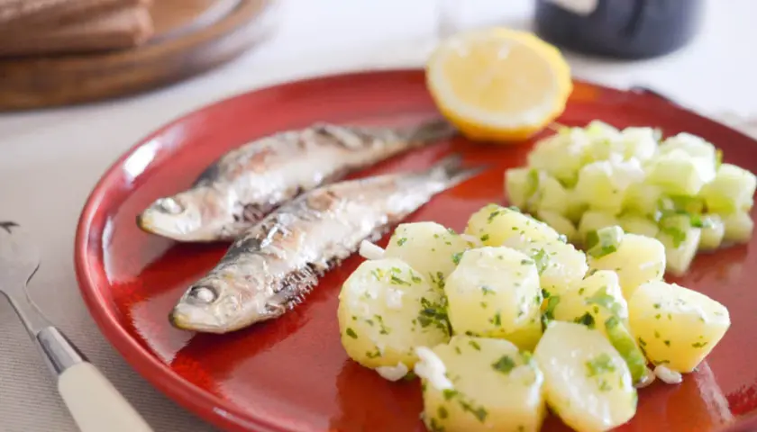 Deux sardines grillées sur une assiette rouge avec une salade de pommes de terre et de concombre. Quel accompagnement avec des sardines grillées !
