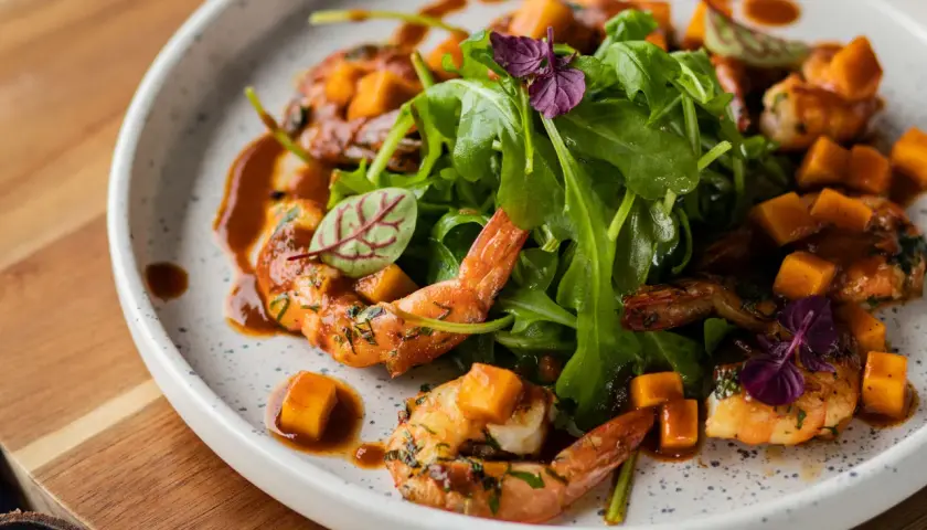 Assiette de crevettes flambées, cubes de mangue et roquette, arrosée d'une sauce caramélisée.