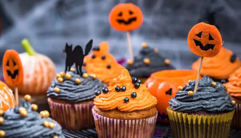 Des muffins d'Halloween effrayants, parfaits pour une recette facile. Glaçage orange et gris, décorés de citrouilles et d'un chat noir.