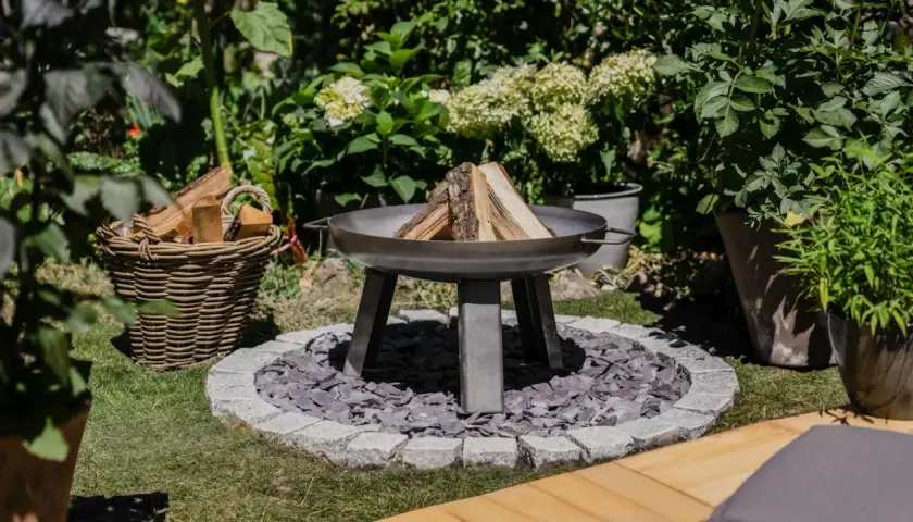Un brasero en forme de chaudron, prêt à être allumé, avec du bois à côté. Un coin de jardin accueillant pour des soirées conviviales.