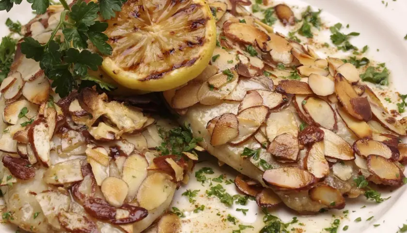 Deux filets de poisson recouverts d'amandes effilées grillées, garni de persil frais et d'une tranche de citron grillée. Un délice de truite aux amandes.