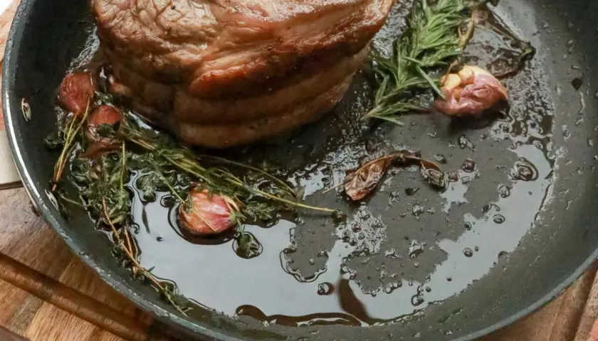 Rouelle de porc au barbecue, dorée et juteuse, mijotant dans une poêle avec de l'ail et des herbes aromatiques.