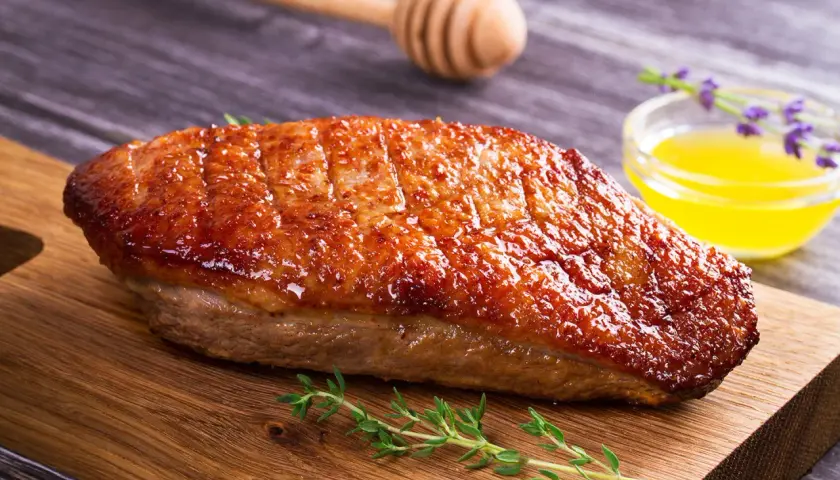 Magret de canard grillé à la perfection, prêt pour la cuisson barbecue gaz. Servi avec une sauce dorée et des herbes fraîches.