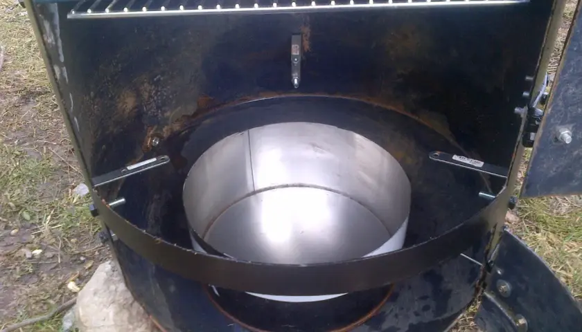 Intérieur d'un fumoir fait maison avec un bidon. Une grille est visible en haut, et un récipient métallique au centre.