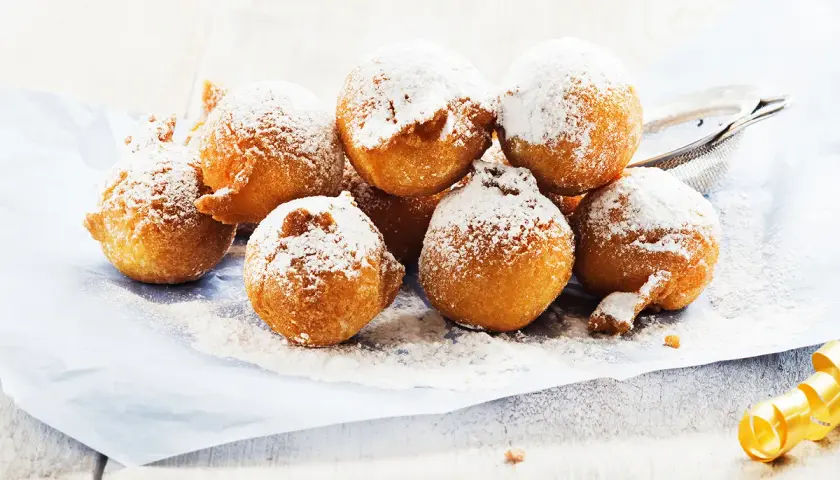 Des beignets dorés saupoudrés de sucre glace, ressemblant à des crottes d'âne, sur du papier bleu.