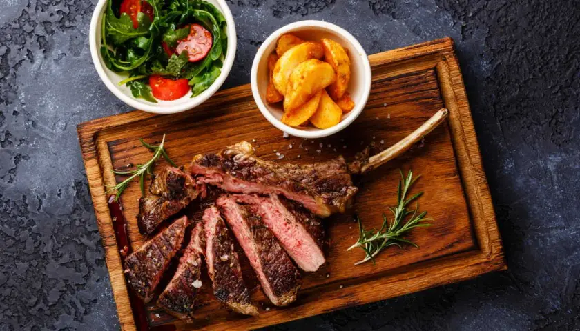Un succulent accompagnement de côte de bœuf, servi avec une salade fraîche et des pommes de terre rôties sur une planche en bois.