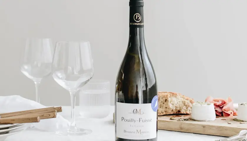Bouteille de Pouilly-Fuissé, deux verres à vin, pain, fromage de chèvre et jambon. Parfait pour une liste boisson mariage.