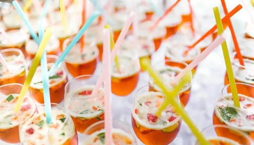 Des verres remplis de cocktails orange vif, garni de fruits et de menthe, avec des pailles colorées. Un parfait cocktail de bienvenue mariage.