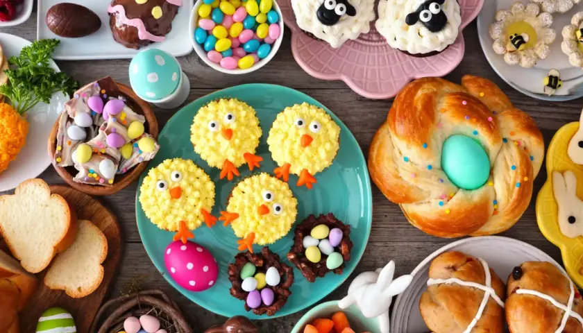 Table garnie de douceurs pascales : cupcakes moutons, poulets, biscuits abeilles, pains tressés, chocolats et bonbons. Parfaites recettes rigolotes pour Pâques !