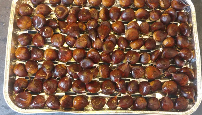 Plateau rempli de châtaignes prêtes à être grillées au barbecue. Elles sont brillantes et bien rangées.