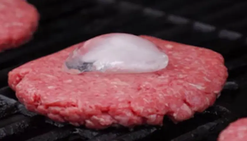 Un steak haché au barbecue, avec un glaçon posé dessus pour une cuisson parfaite.