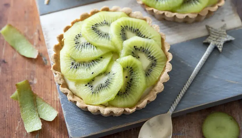 Délicieux dessert kiwi, une tartelette garnie de crème et de fines rondelles de kiwi, prête à être dégustée.