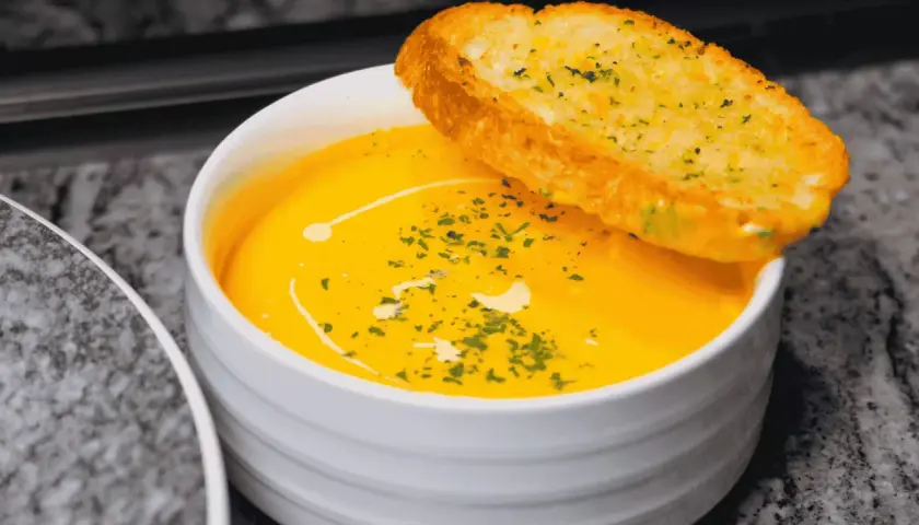 Soupe orange onctueuse, garnie d'herbes et d'un filet de crème, avec une tranche de pain à l'ail. Idéal pour savoir comment épaissir une soupe.