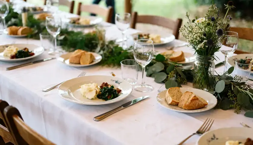 Un repas simple et champêtre, parfait pour une idée repas lendemain mariage. Des assiettes dressées avec purée, légumes verts et pain frais, entourées de verdure et de fleurs sauvages.