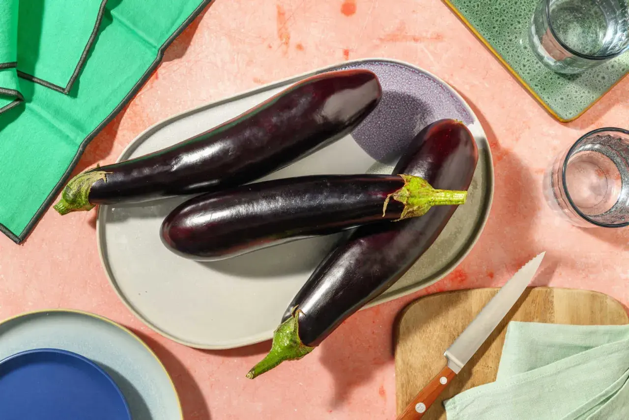 Trois aubergines allongées sur une assiette, prêtes pour des recettes d'été. Ces légumes de juin promettent de délicieux plats.