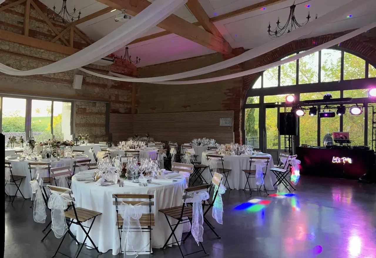 Salle de réception décorée pour un mariage de 80 personnes, tables dressées, lumières d'ambiance et DJ prêt à animer la soirée.