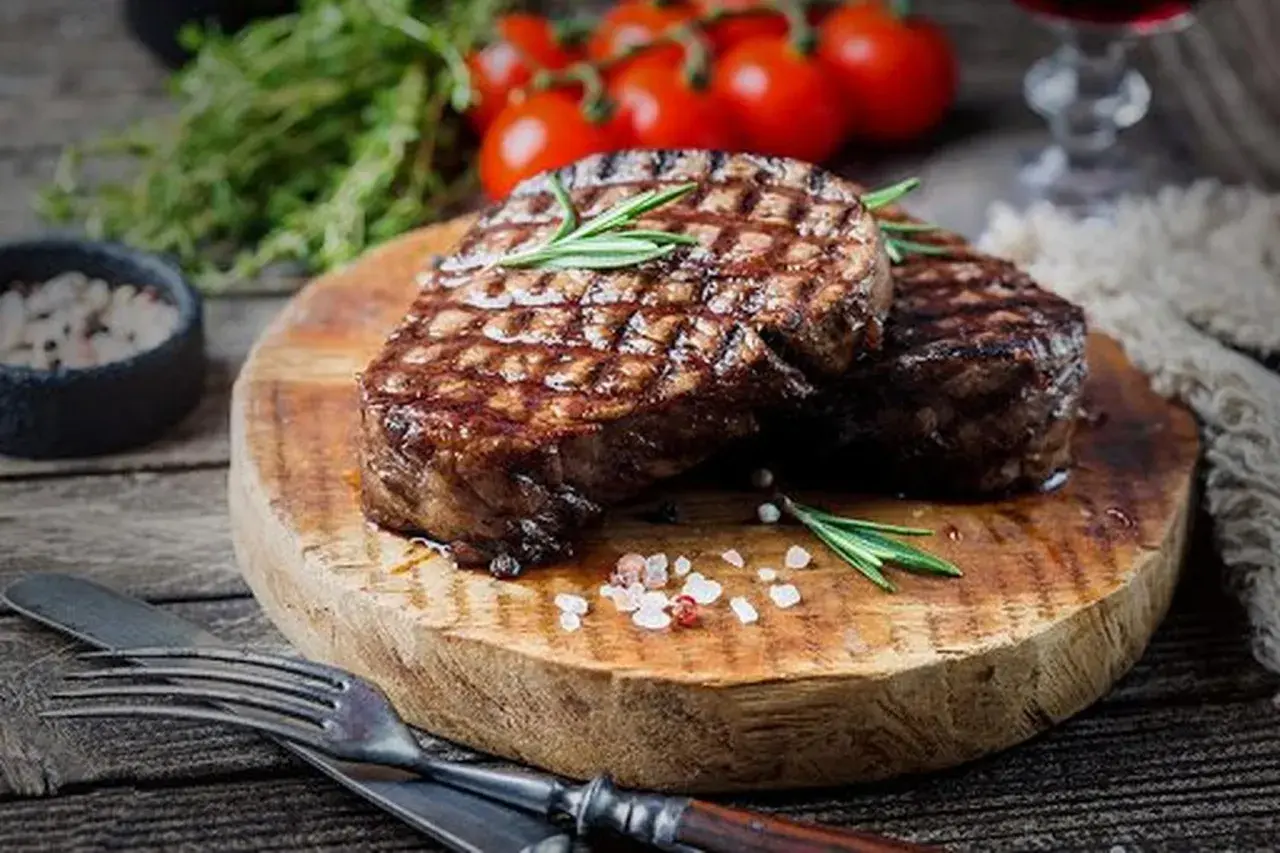 Deux steaks grillés sur une planche en bois, parsemés de gros sel rose. Une question se pose : quand saler la viande au barbecue pour un résultat parfait ?