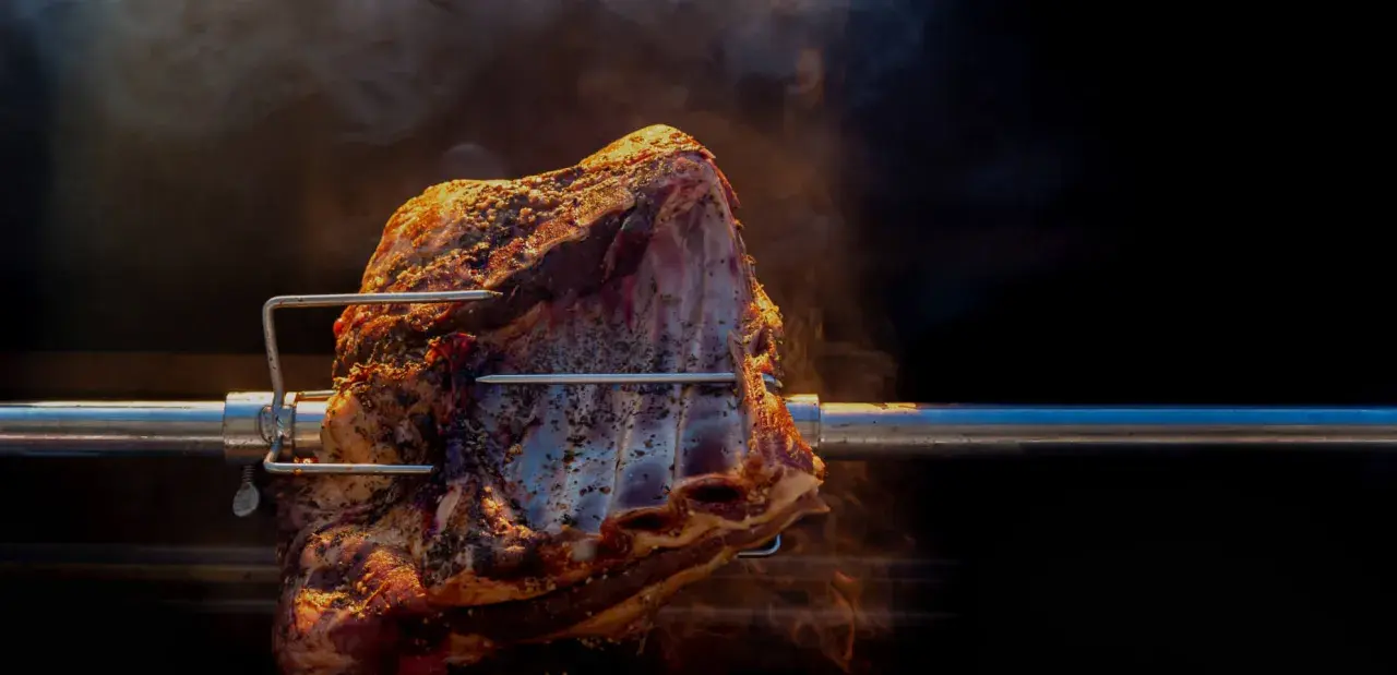 Un morceau de viande assaisonné tourne lentement sur une broche, dégageant une fumée alléchante. La cuisson à la broche promet un délice savoureux.