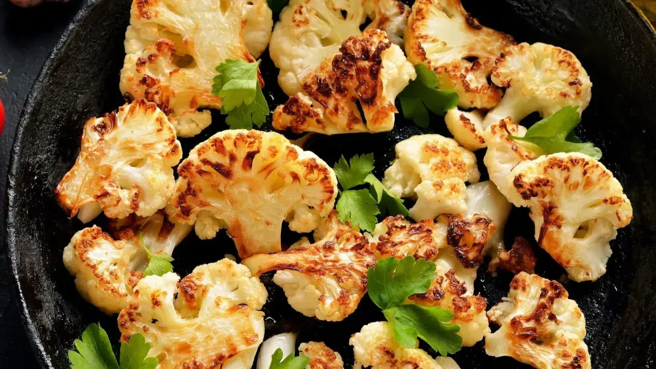 Tranches de chou-fleur rôti au four, dorées et caramélisées, garnies de persil frais dans une poêle en fonte.