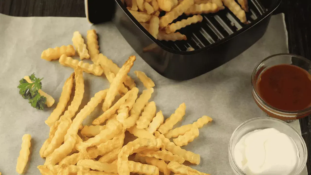 Frites maison ondulées, croustillantes et dorées, tout juste sorties de l'airfryer Ninja. Servies avec ketchup et mayonnaise.