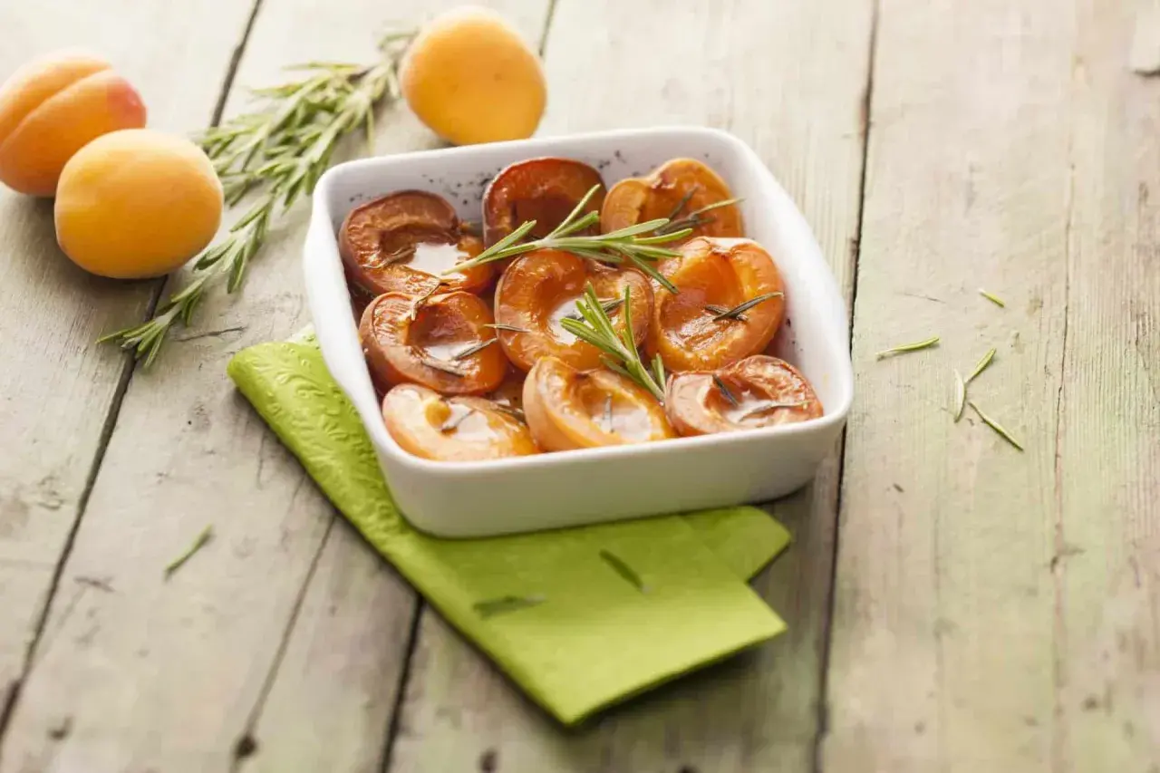 Abricots rôtis au four, tendres et caramélisés, garnis de romarin frais. Un délice simple et parfumé.