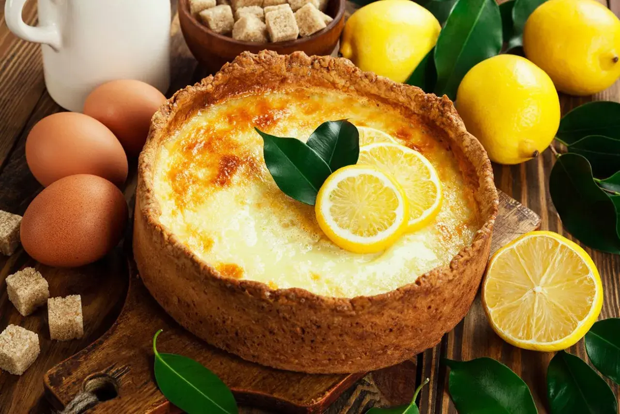 Un délicieux flan au citron, garni de rondelles de citron et de feuilles vertes, entouré de citrons frais, d'œufs et de sucre.