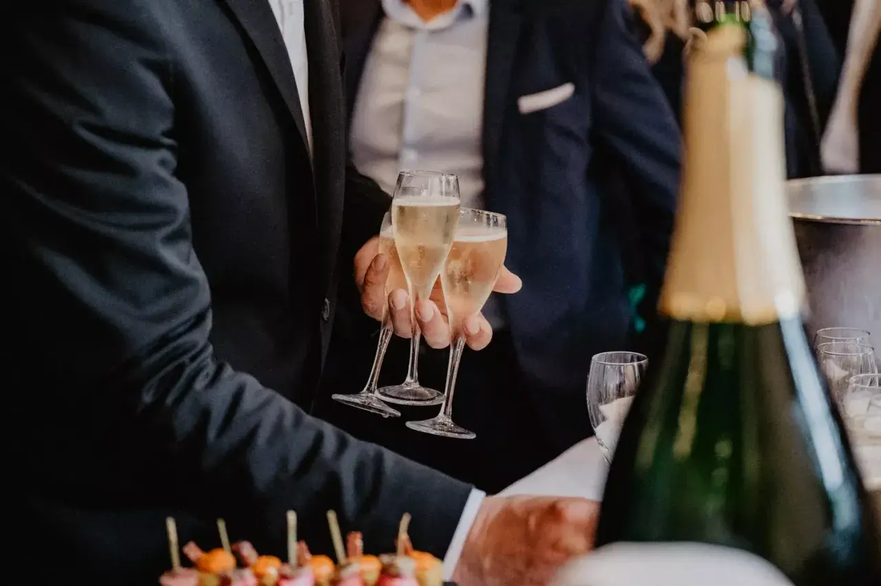 Des flûtes de champagne pétillant pour le vin d'honneur mariage. Des canapés colorés et une bouteille de champagne en avant-plan.
