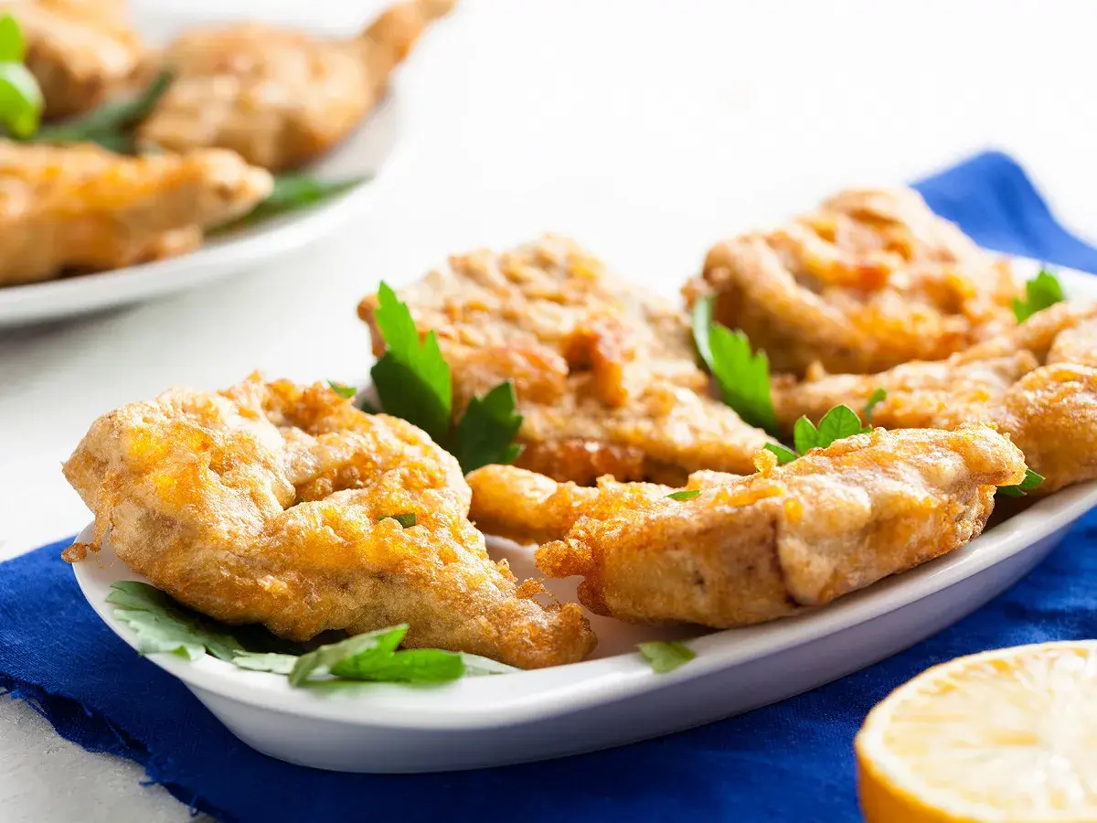 Délicieux artichaut frit, croustillant et doré, servi sur une assiette blanche avec des herbes fraîches et un quartier de citron.