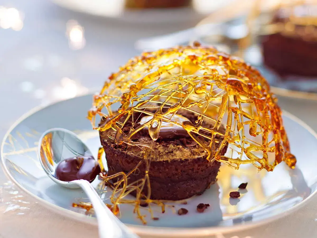 Gâteau au chocolat surmonté d'une décoration caramel facile et aérienne, avec une cuillère de sauce au chocolat.