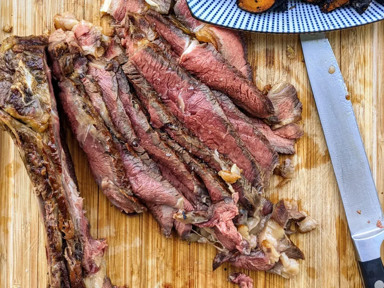 Tranches de bœuf juteuses, parfaitement cuites par la méthode du reverse searing, sur une planche en bois. Un couteau est à côté.