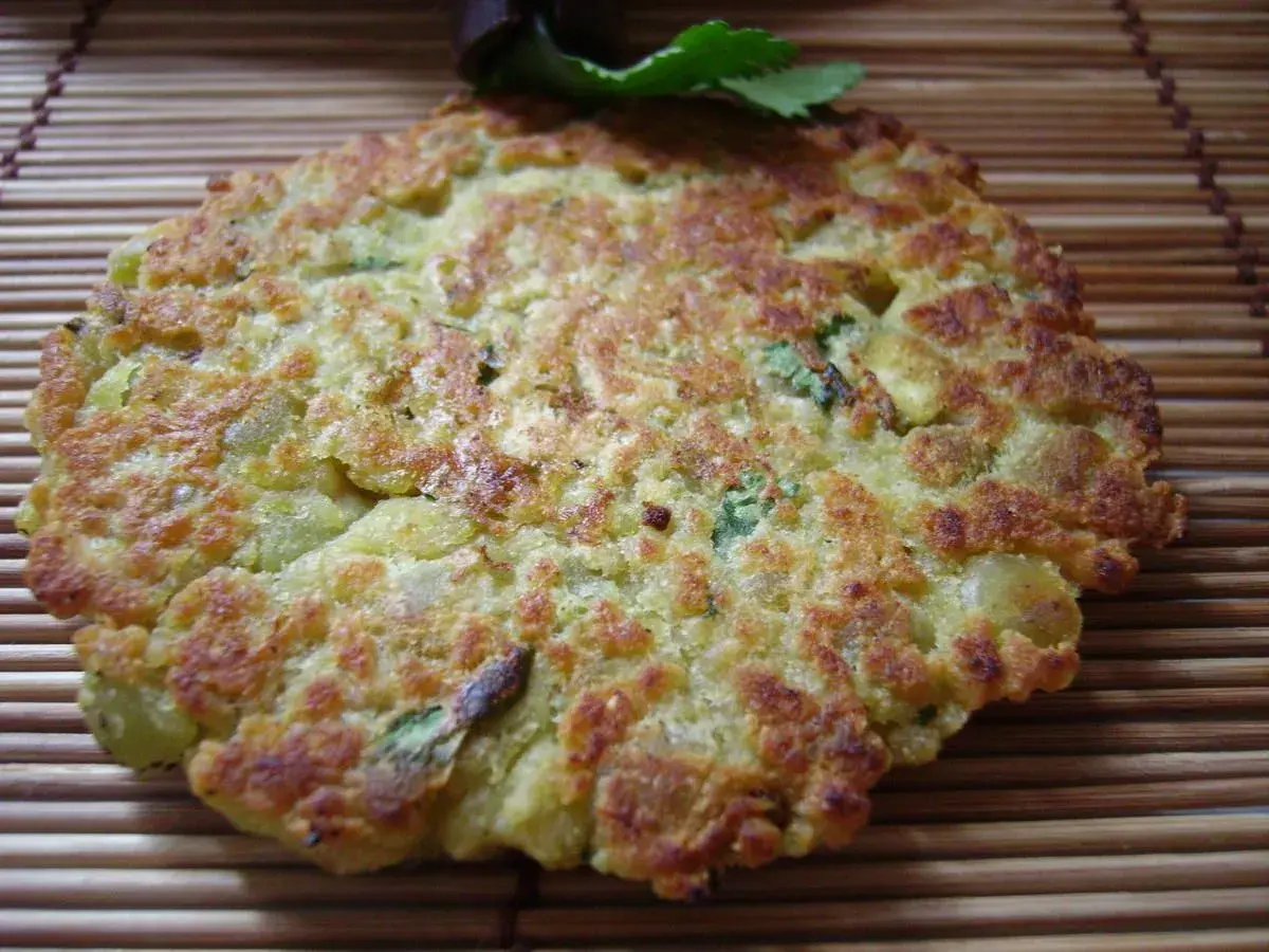 Une galette de pois cassés dorée et croustillante, garnie de persil frais, repose sur un tapis de bambou.