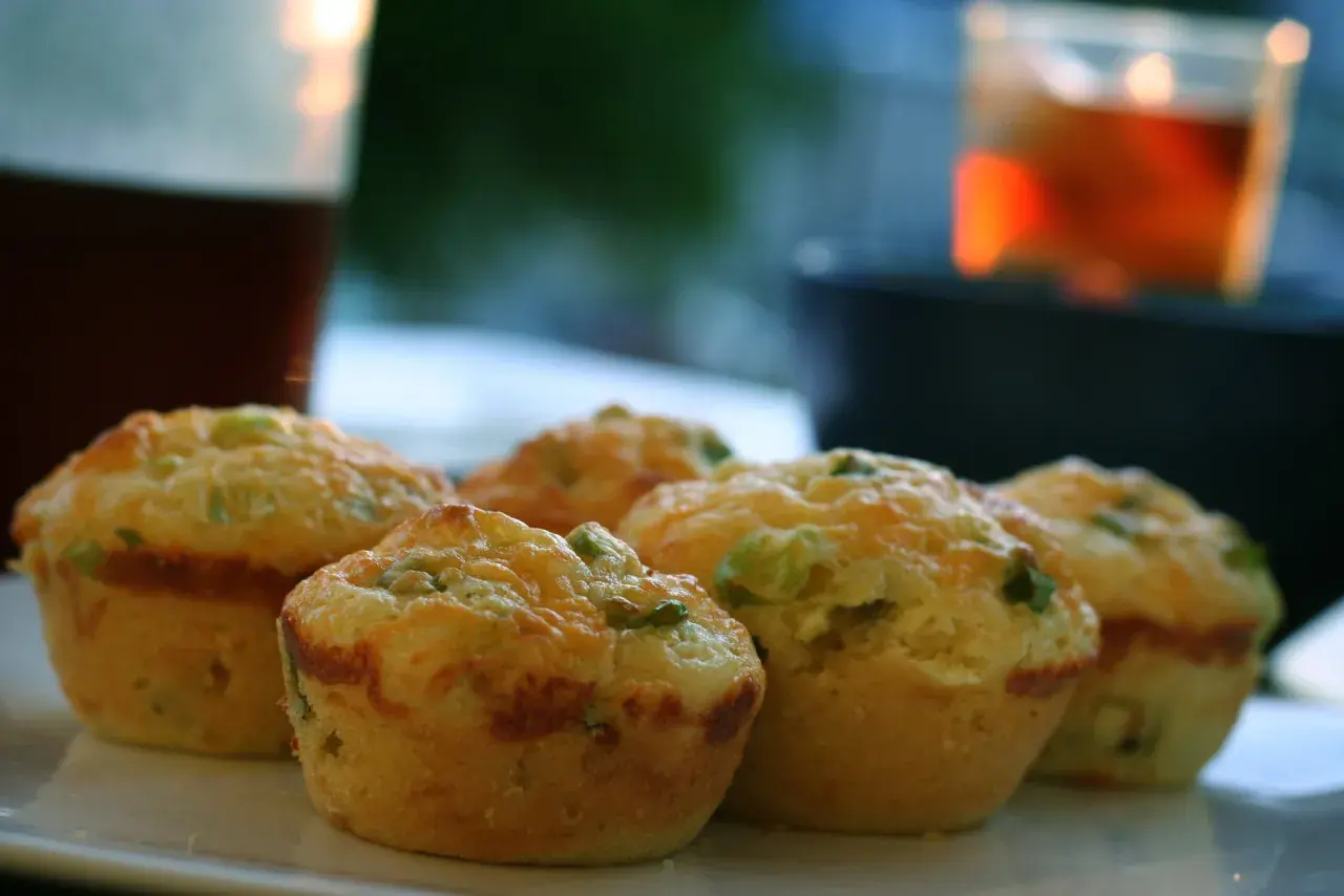 Cinq muffins salés dorés, garnis de fromage et d'herbes, sur une assiette blanche.