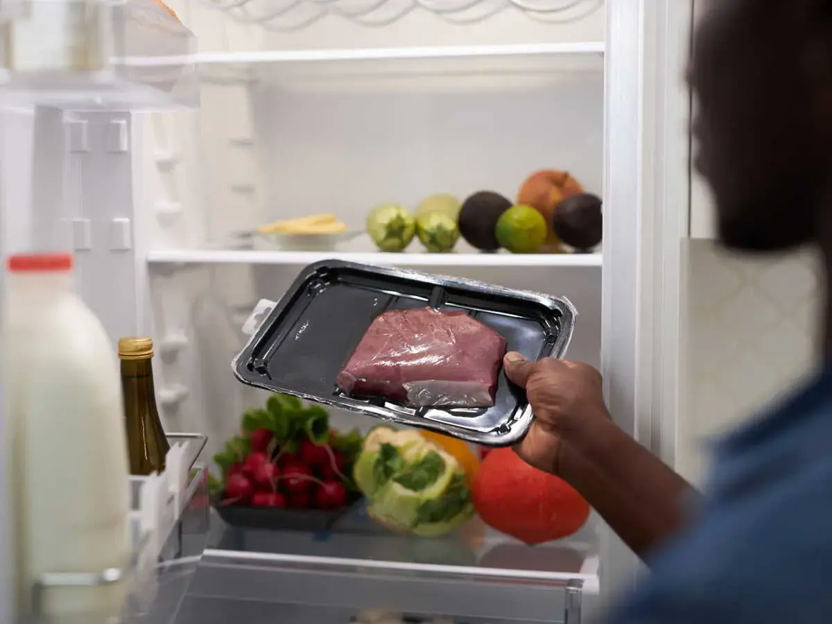 Un homme regarde un morceau de viande dans son emballage. Il se demande : viande hors frigo combien de temps ?