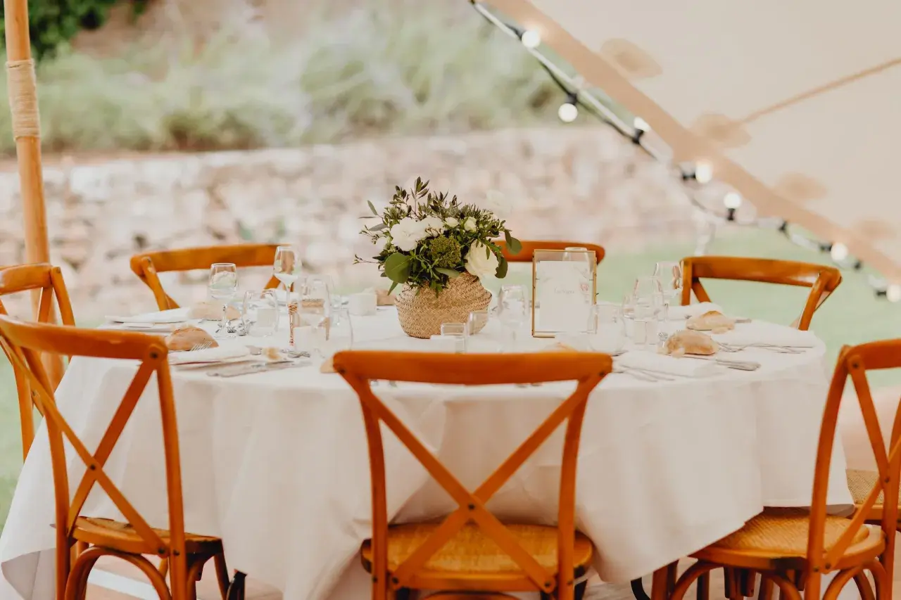 Table dressée pour un repas traditionnel mariage français, avec des chaises en bois, des fleurs et des petits pains.