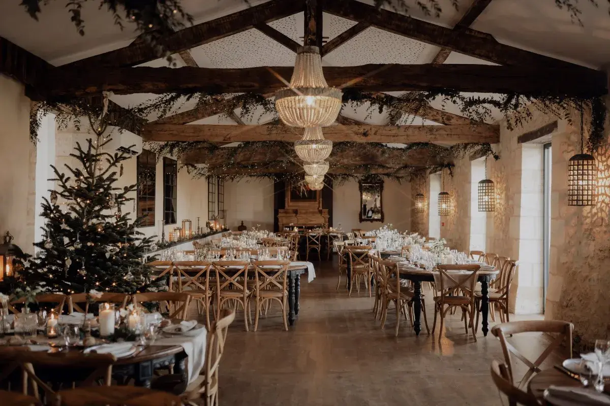 Une salle de réception décorée pour un mariage en hiver, avec un sapin illuminé, des guirlandes lumineuses et des tables dressées.