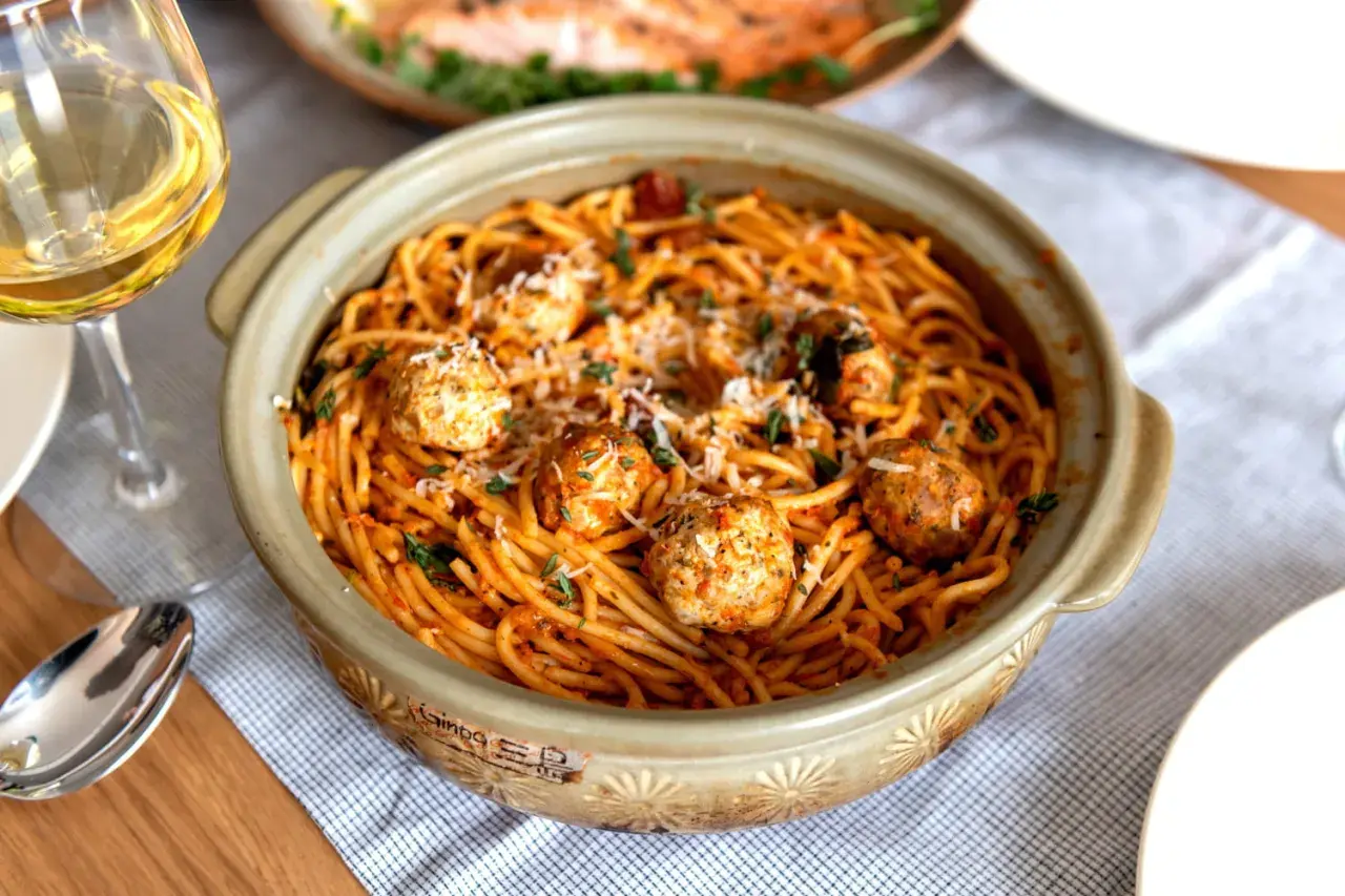 Spaghetti aux boulettes de viande dans un plat en céramique, parsemé de parmesan et d'herbes. Une recette facile et gourmande parfaite pour un repas convivial.